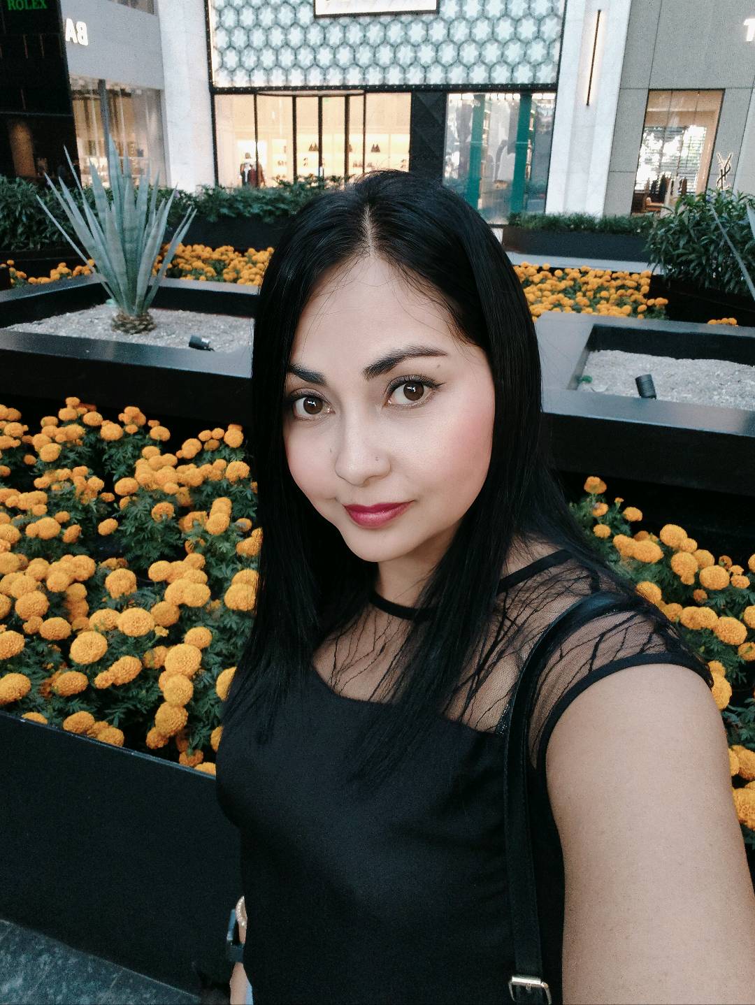 Smiling woman in a black top taking a selfie outdoors, ready for a video call