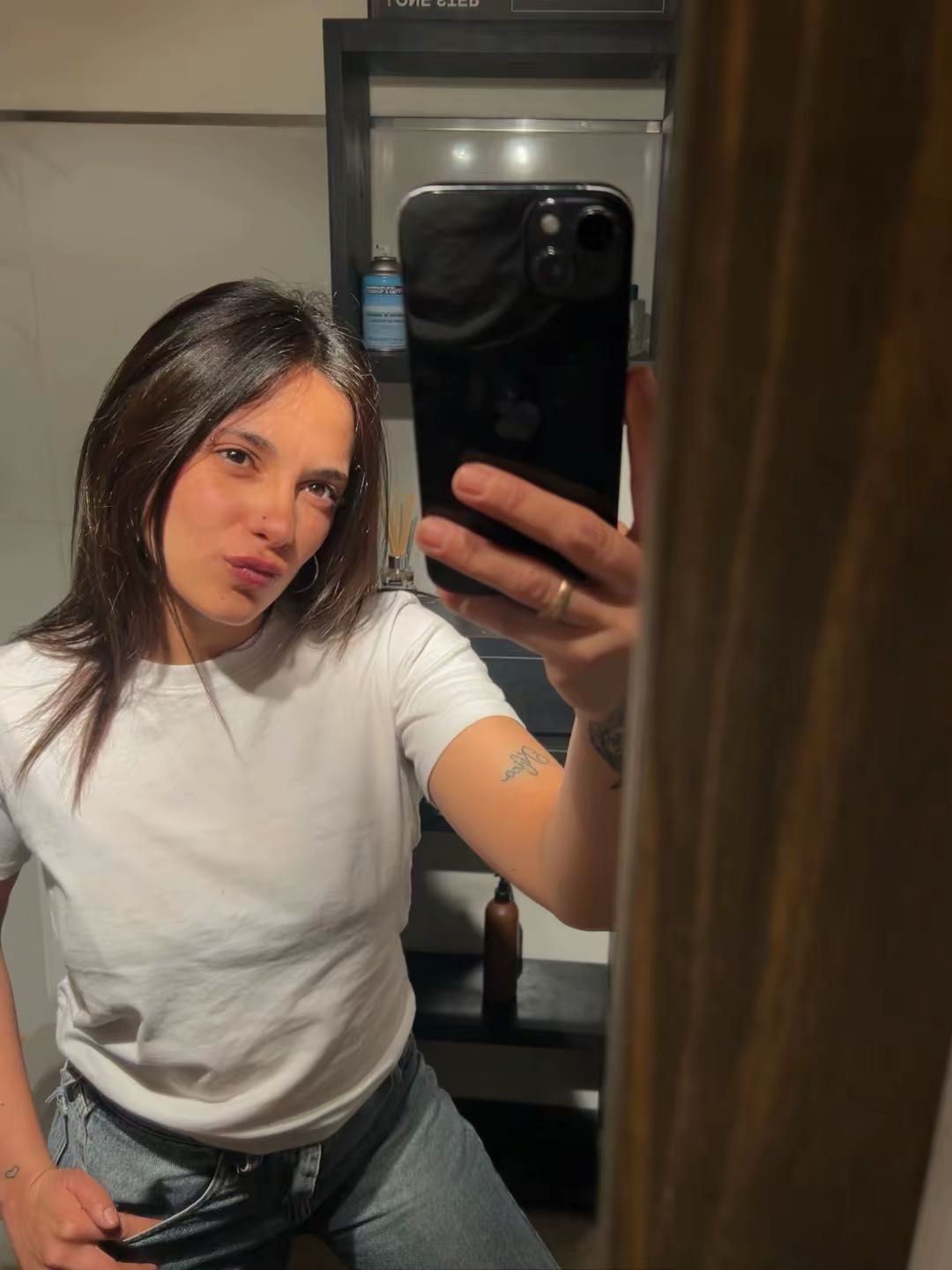 Woman in a white T-shirt taking a mirror selfie at home before a private call